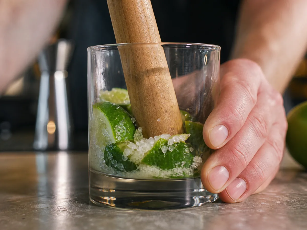 Limettenstücke und Zucker werden vorsichtig im Glas angedrückt
