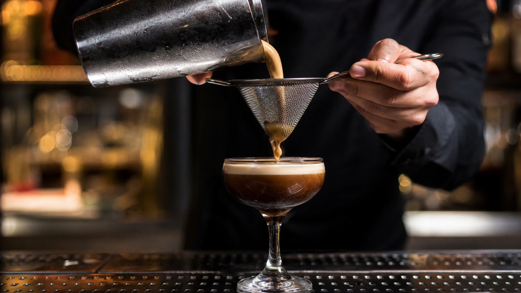 Dunkler Cocktail wird durch ein Feinsieb in ein gekühltes Glas gegossen