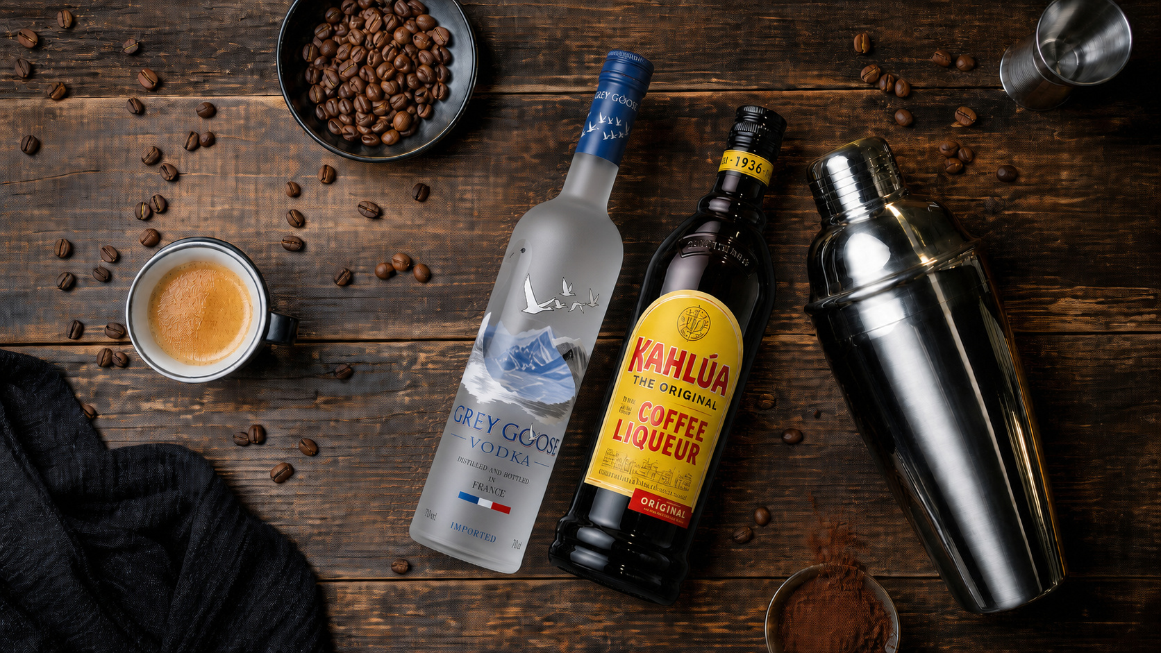 Flatlay mit Grey Goose Wodka, Kahlúa Kaffeelikör, Shaker und Espressotasse auf dunklem Holztisch