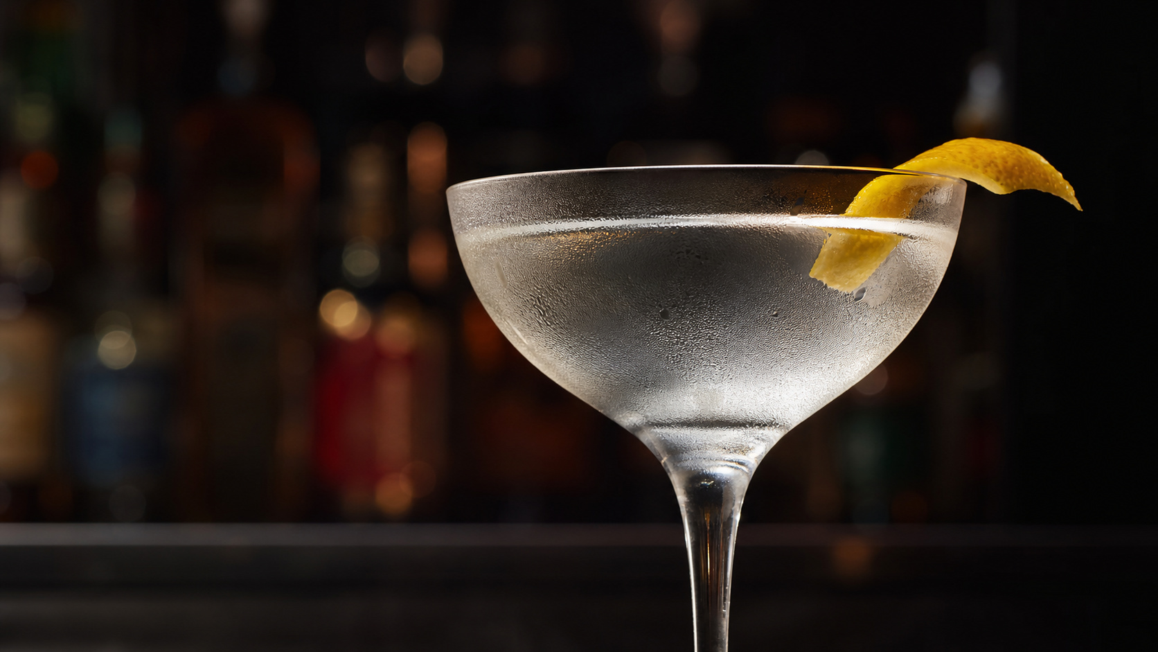 Eiskalter Wodka Martini in einem beschlagenen Martiniglas mit Zitronenzeste vor dunklem Barhintergrund