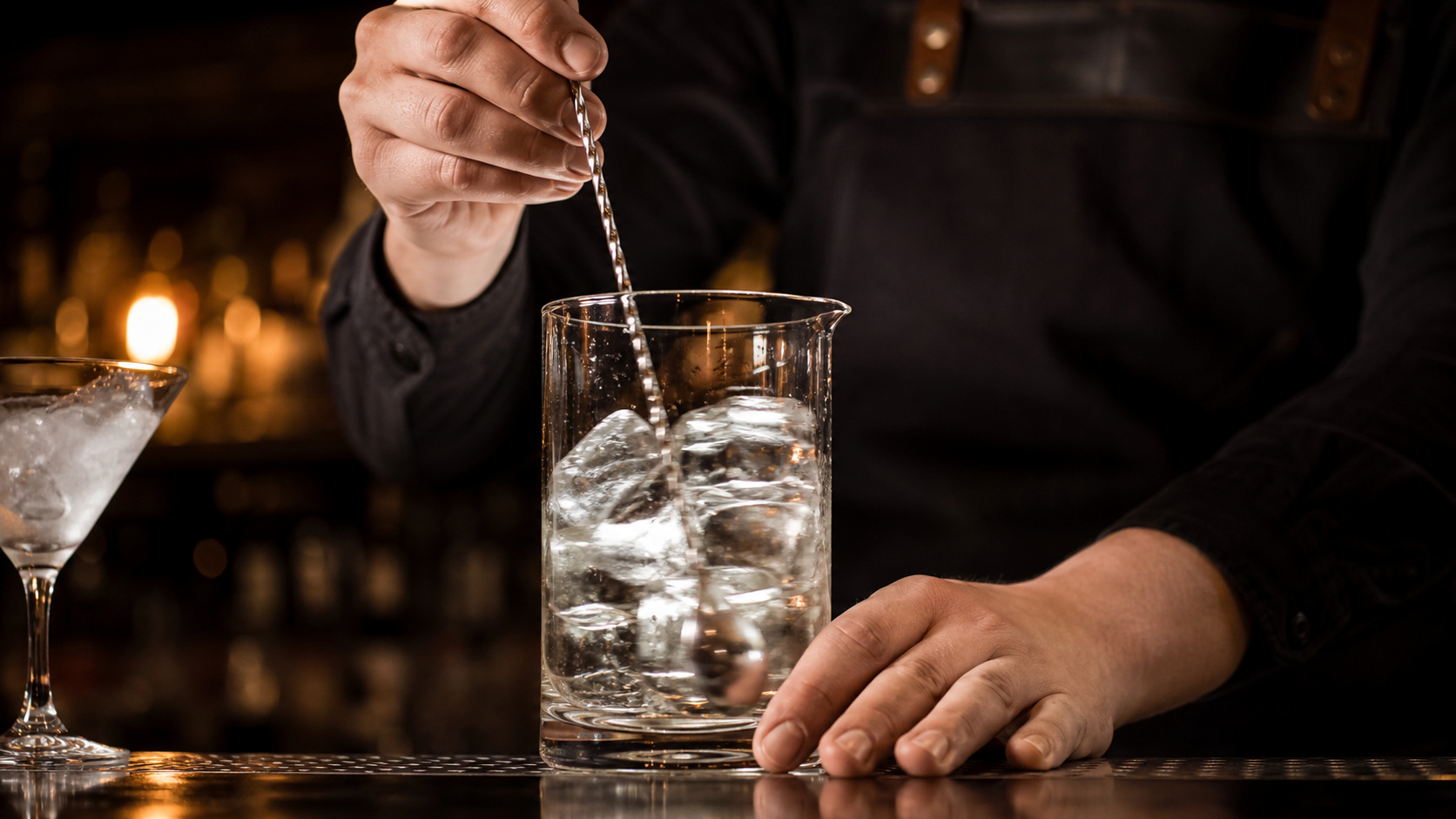 Barkeeper rührt einen Martini mit einem langen Barlöffel in einem Rührglas mit klaren Eiswürfeln