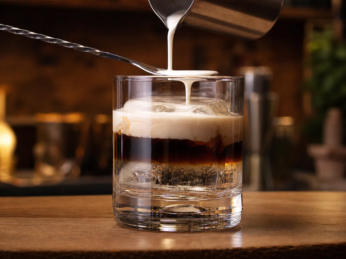 Sahne wird über einen Barlöffel auf einen White Russian gegossen